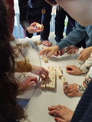 Das Bild zeigt viele verschiedene Hände, die auf einem Tisch Spielsteine zusammenlegen.