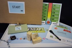 Das Bild zeigt den Spielkarton der Spiels "Escape Climate Change" mit einigen Materialien aus dem Spiel.