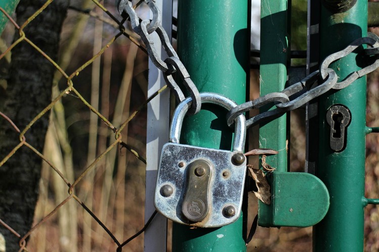 Vorhängeschloss an einer Kette an einer Tür im Zaun