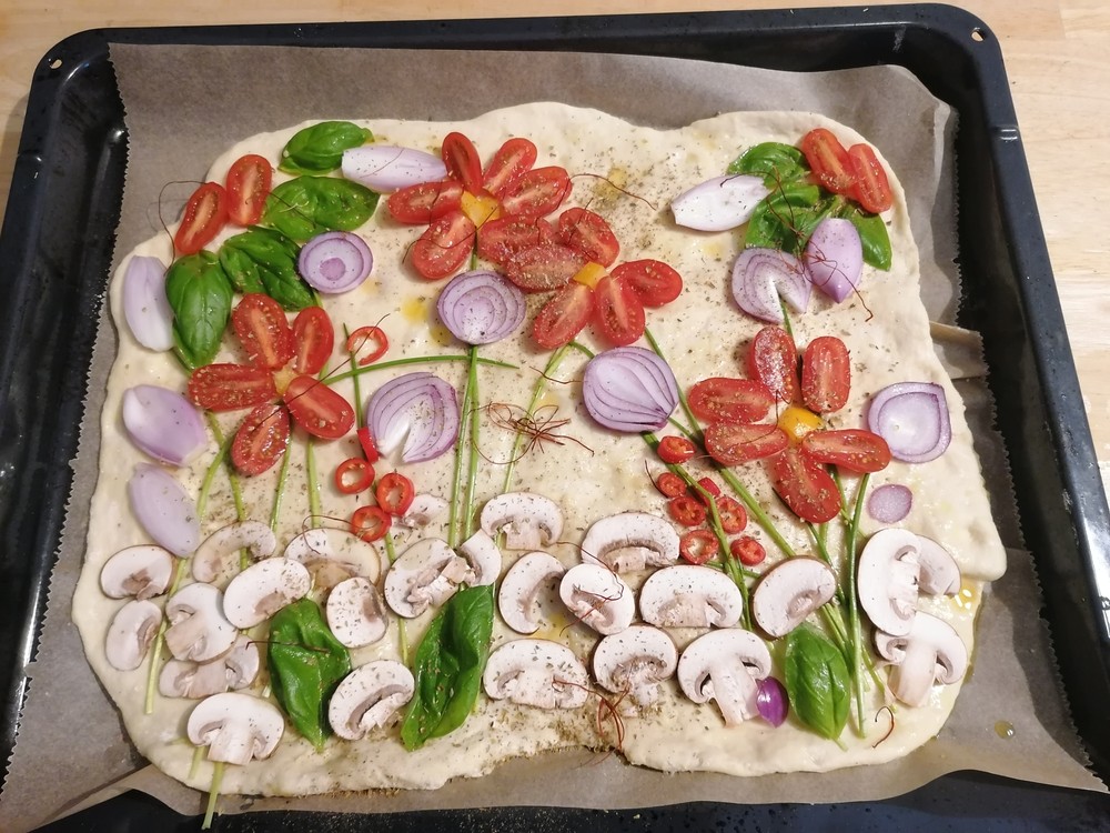 Das Bild zeigt eine Pizza, deren Zutaten als Blumenwiese arrangiert sind.