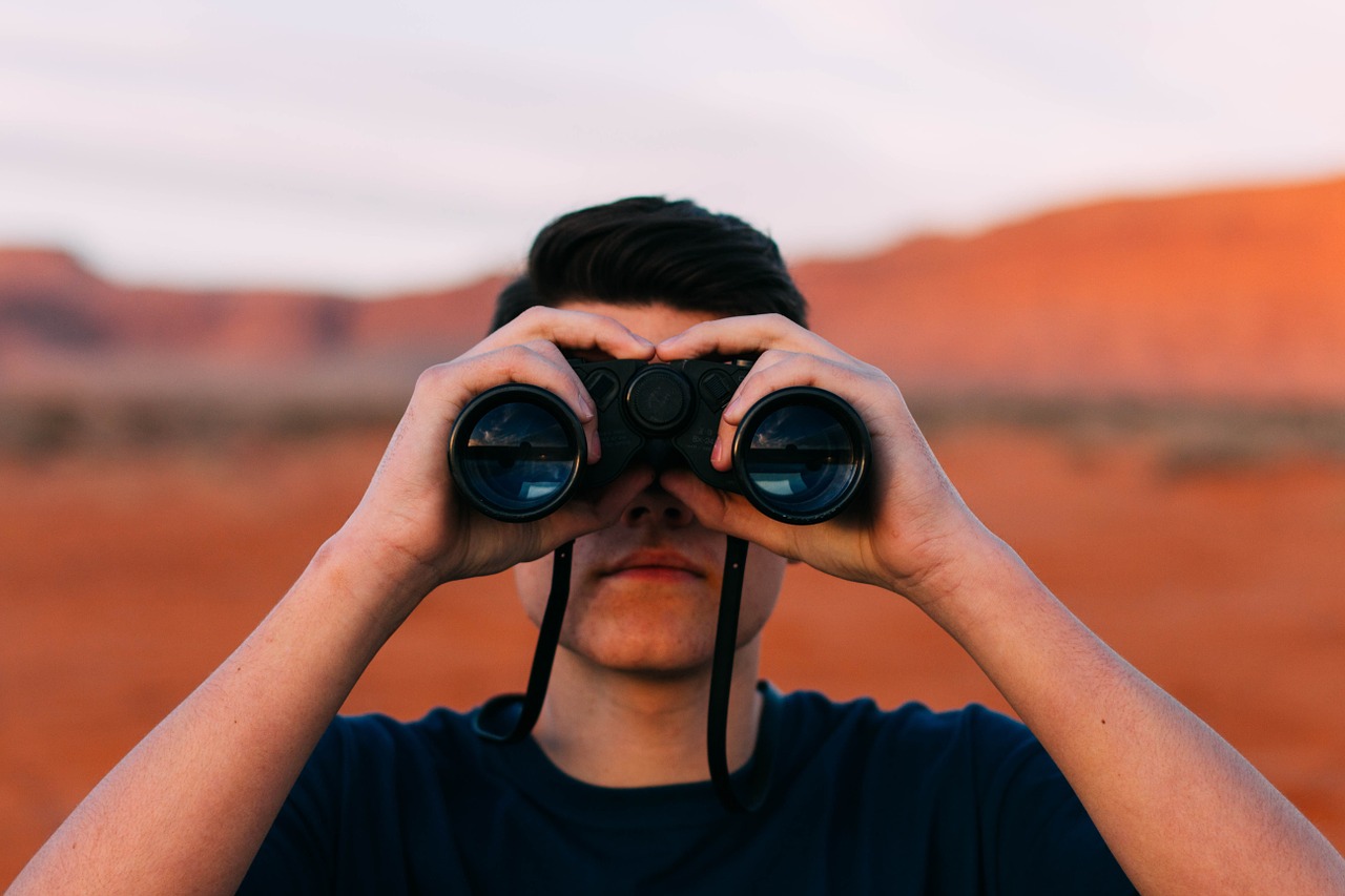 Mann in einer Landschaft schaut durch ein Fernglas.