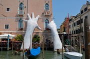 Das Bild zeigt ein Kunstobjekt in Venedig, zwei Hände greifen nach einem Haus.